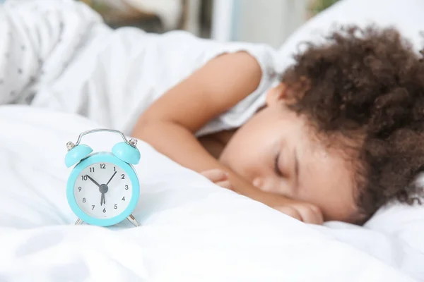 Little African-American girl with alarm clock sleeping in bed — Stock Photo, Image