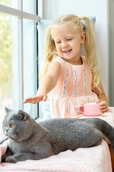 Μικρό κορίτσι με χαριτωμένο γάτα κοντά στο παράθυρο — Φωτογραφία Αρχείου