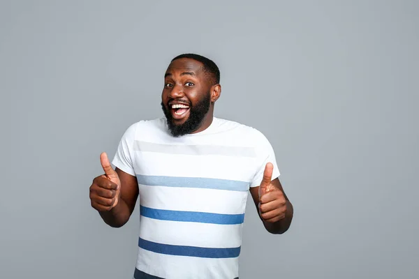 Hombre afroamericano guapo mostrando gesto de pulgar hacia arriba sobre fondo gris — Foto de Stock