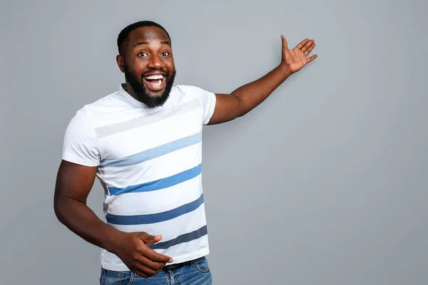 Feliz hombre afroamericano mostrando algo sobre fondo gris —  Fotos de Stock