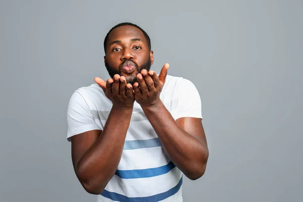 Handsome African-American man blowing kiss on grey background — Stock Photo, Image