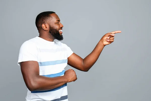 Happy African-American man pointing at something on grey background