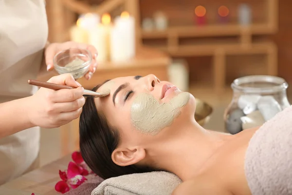 Cosmetologo che applica maschera su faccia di giovane donna in salone di centro benessere — Foto Stock
