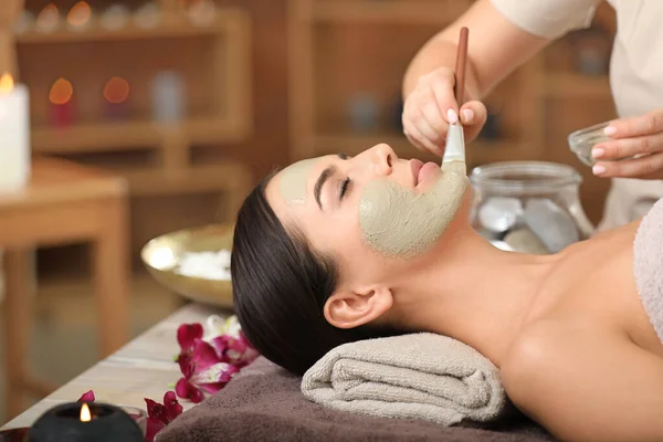 Cosmetologist aplicando máscara no rosto da jovem mulher no salão de spa — Fotografia de Stock