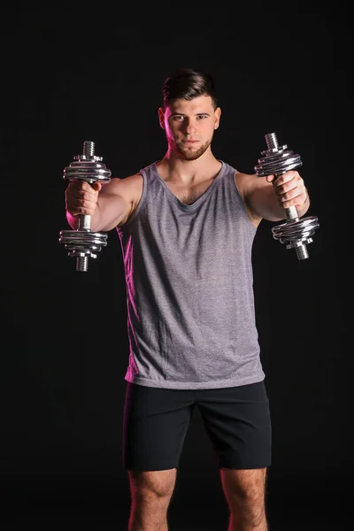 Jeune homme sportif avec haltères sur fond sombre — Photo