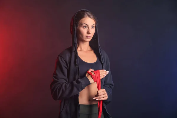 Sporty young woman applying wrist bands on dark background — Stock Photo, Image