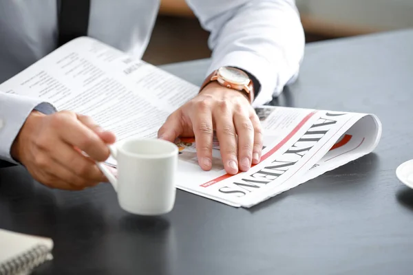 Handsome businessman drinking coffee while reading newspaper in office, closeup — ストック写真