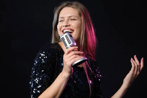 Linda jovem cantora com microfone no fundo escuro — Fotografia de Stock