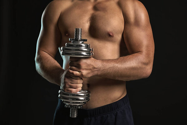 Handsome male bodybuilder with dumbbell on dark background