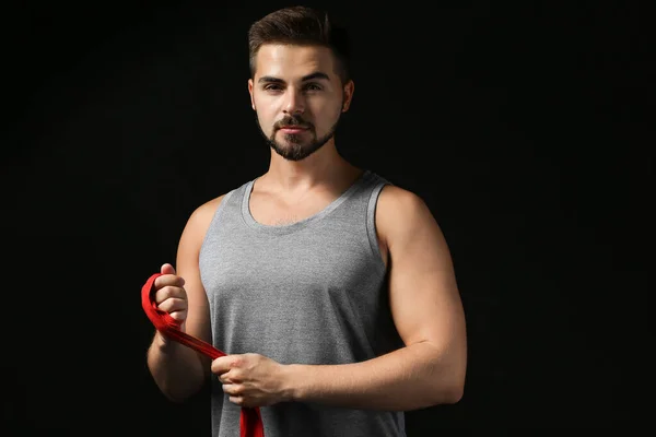 Sporty young man applying wrist bands against dark background — Stock Photo, Image