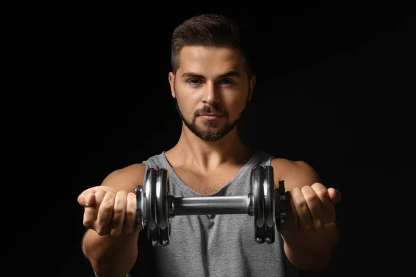 Jeune homme sportif avec haltère sur fond sombre — Photo