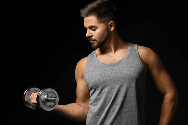 Sporty young man with dumbbell on dark background — Stock Photo, Image