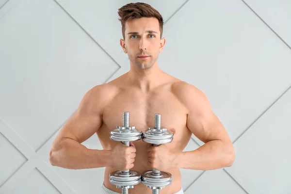 Sporty young man with dumbbells on light background — Stock Photo, Image