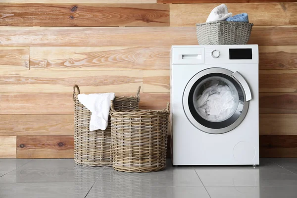 Modern tvättmaskin med tvätt nära trävägg — Stockfoto