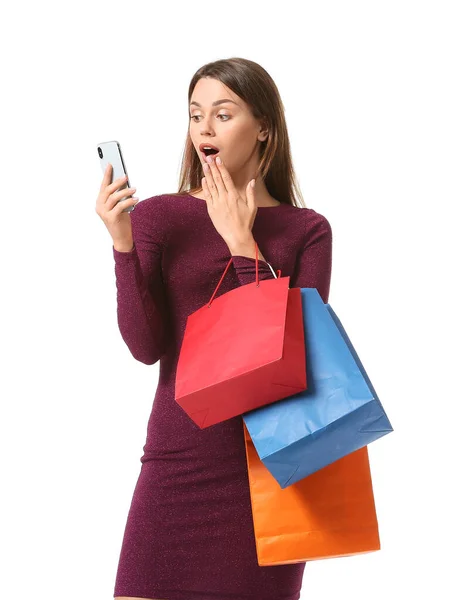 Překvapená mladá žena s nákupními taškami a mobilním telefonem na bílém pozadí — Stock fotografie