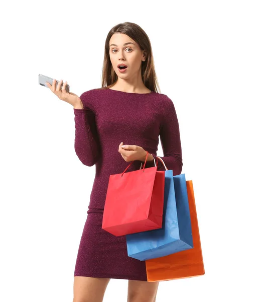 Verrast jonge vrouw met boodschappentassen en mobiele telefoon op witte achtergrond — Stockfoto