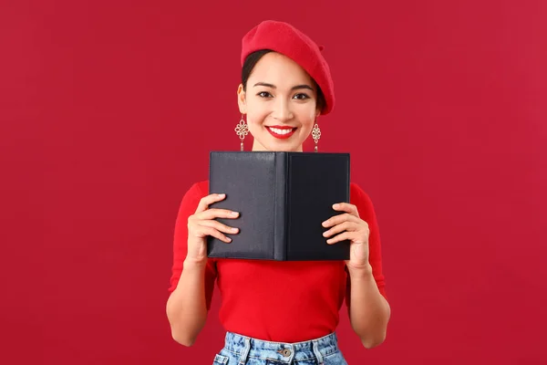 Fashionable Asian woman with book on color background — Stock Photo, Image