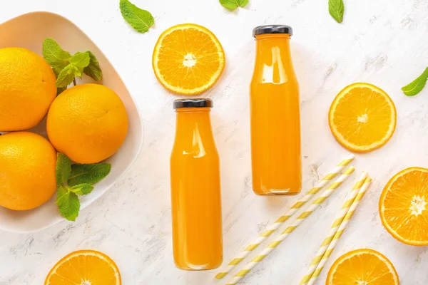 Bottles of fresh orange juice on light table — Stock Photo, Image