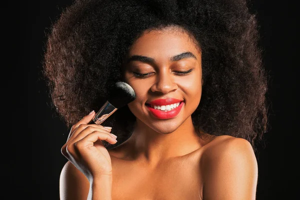 Portrét krásné afroamerické ženy s make-up štětce na tmavém pozadí — Stock fotografie