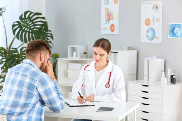 Médico femenino trabajando con triste paciente masculino en clínica —  Fotos de Stock