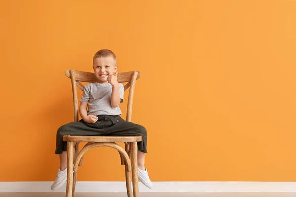 Retrato de lindo niño sentado en la silla y mostrando el gesto de pulgar hacia arriba contra el fondo de color — Foto de Stock
