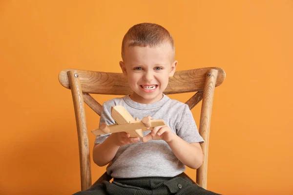 Retrato de lindo niño con juguete sentado en la silla contra el fondo de color — Foto de Stock