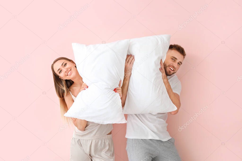 Young couple with pillows on color background