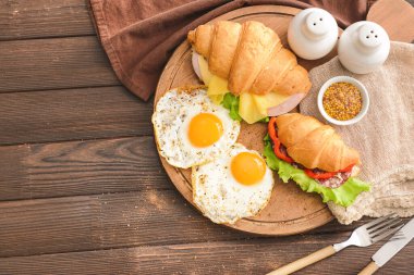 Lezzetli kruvasan sandviçler ve ahşap masada kızarmış yumurtalar.