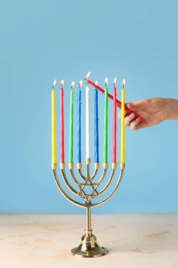 Woman lighting candles in menorah for Hanukkah on color background clipart
