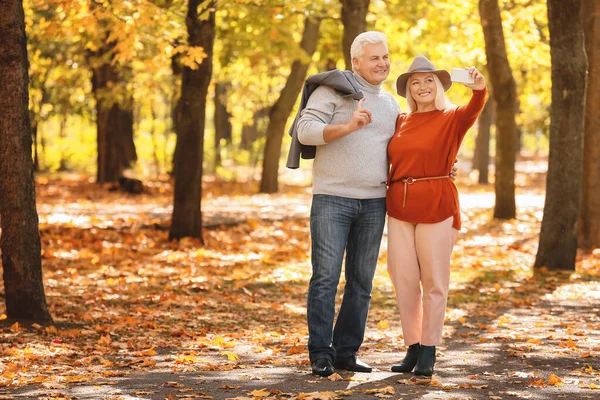 Loving mature couple taking selfie in autumn park — Stock Photo, Image