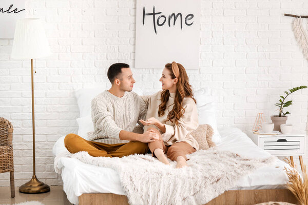 Beautiful young couple sitting on bed at home