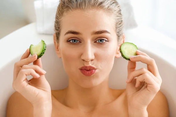 Hermosa mujer joven con rodajas de pepino tumbado en el baño —  Fotos de Stock