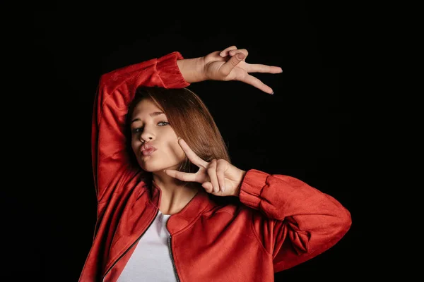 Funny teenage girl showing victory gesture on dark background