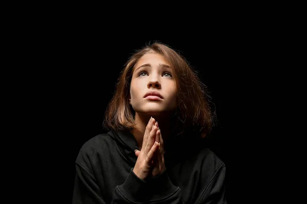 Sad teenage girl praying against dark background — Stock Photo, Image