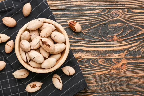 Bowl with tasty pecan nuts on wooden background