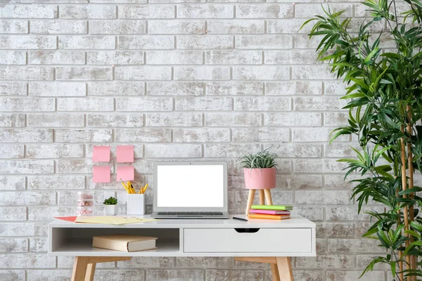 Moderno lugar de trabajo elegante con ordenador portátil cerca de pared de ladrillo — Foto de Stock