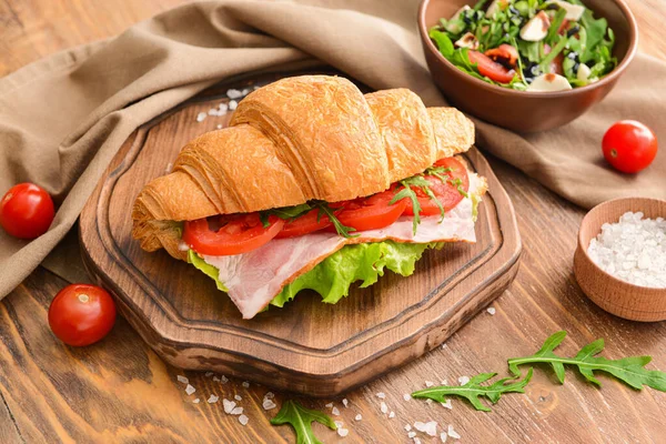 Brett mit leckerem Croissant-Sandwich auf Holztisch — Stockfoto