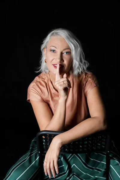 Retrato de mulher madura elegante mostrando gesto de silêncio no fundo escuro — Fotografia de Stock