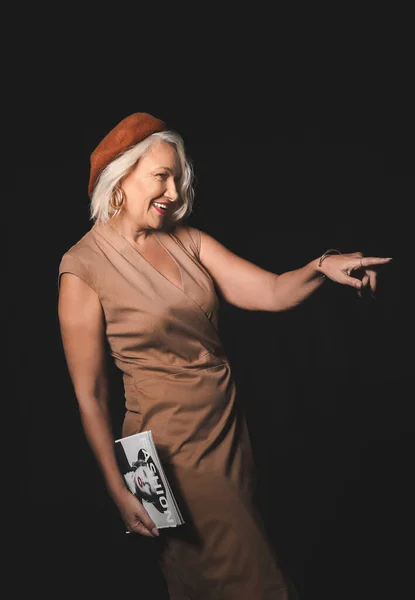 Portrait of stylish mature woman with fashion magazine on dark background — Stock Photo, Image