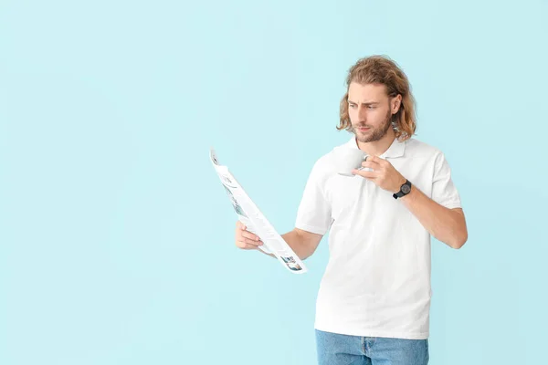 Portrait of handsome man with newspaper and cup of coffee on color background — Stock Photo, Image