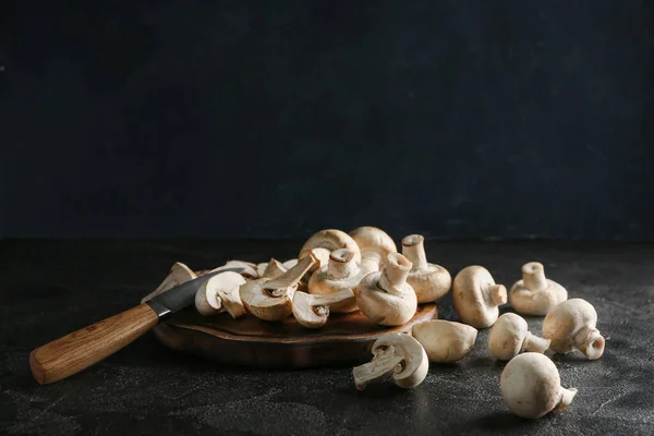 Planche à découper avec champignons frais et couteau sur fond sombre — Photo