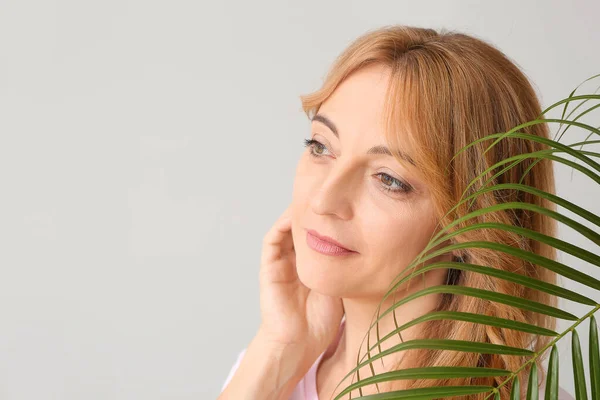 Mature woman with tropical leaf on light background — Stock Photo, Image