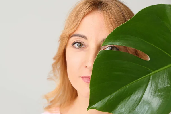 Volwassen vrouw met tropisch blad op lichte achtergrond — Stockfoto