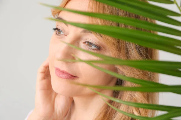 Mature woman with tropical leaf on light background — Stock Photo, Image