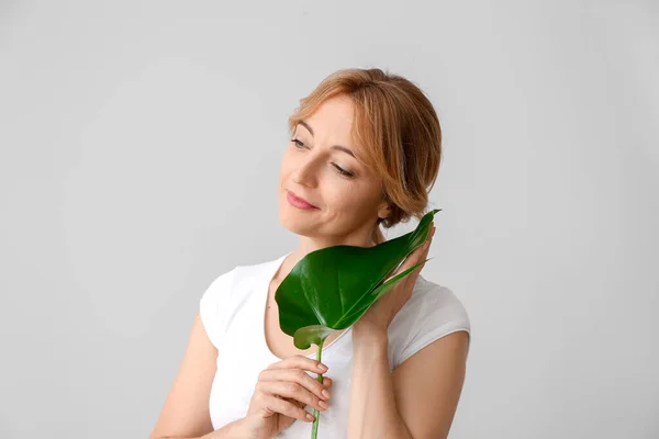 Mature woman with tropical leaf on light background — Stock Photo, Image