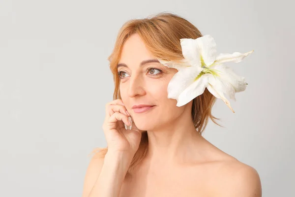 Volwassen vrouw met bloem in haar haar op lichte achtergrond — Stockfoto