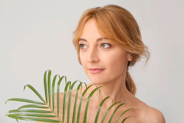 Mature woman with tropical leaf on light background — Stock Photo, Image