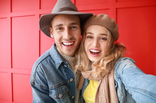 Счастливая молодая пара в теплой осенней одежде делает селфи на цветном фоне — стоковое фото