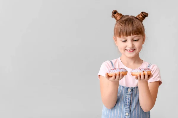 Cute little girl with donuts on light background — Stock Photo, Image