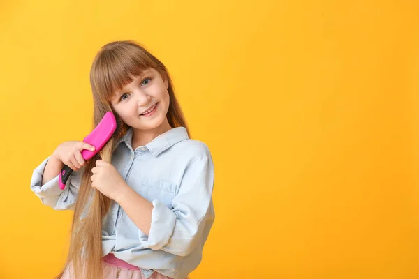 Cute little girl brushing hair on color background — Stock Photo, Image